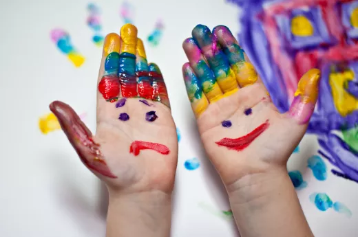 Das Bild zeigt zwei Kinderhände, die mit der handfläche nach oben zeigen. Die Hände sind bunt bemalt. Auf der rechten Hand ist ein föhliches Gesicht zu ehen, auf der linken Hand ein trauriges. 